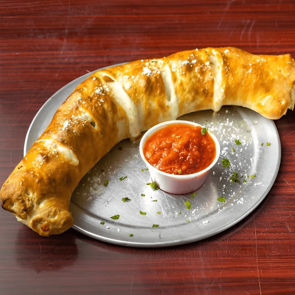 A golden-brown stromboli, dusted with cheese and herbs, served with a side of marinara sauce on a metal plate.