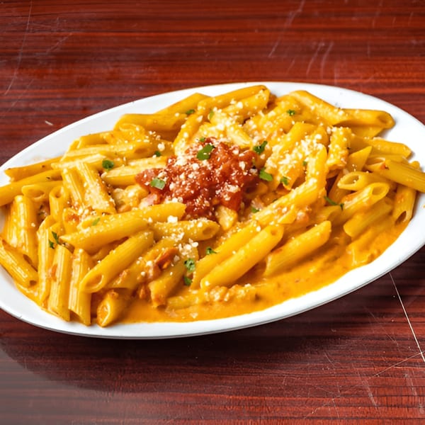 A white oval plate filled with penne pasta in a creamy orange sauce, topped with red marinara and cheese.