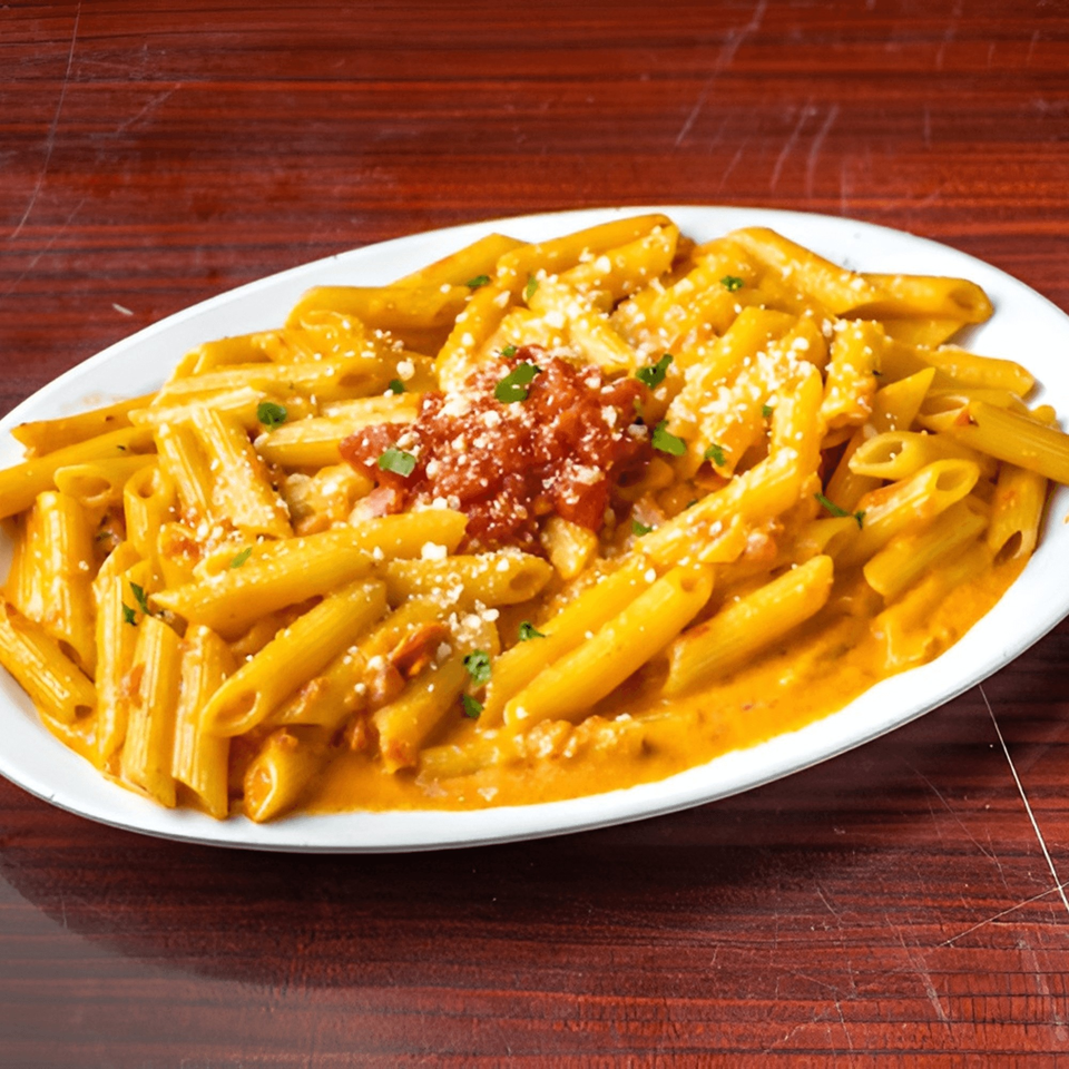 A white oval plate filled with penne pasta in a creamy orange sauce, topped with red marinara and cheese.